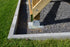 Close-up of a wooden post secured with a metal bracket and 1/4x3 Galv. Hex Head Lag Screws (4 pcs) on a gravel base, surrounded by a concrete border on grass.