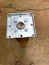 A top view shows a Titan Wood Post Anchor secured to a wooden post using four 1/4x4 Galv. Hex Head Lag Screws from an 8-piece set. The bracket has multiple holes and a central opening exposing the wood beneath. In the background, a concrete surface contrasts with an orange cable.