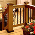 The wooden deck features black metal railings fastened with #14x4 Black Flat Head Screws. Red and white flowers in planters add charm, while a chair and table create a cozy atmosphere, all supported by sturdy Titan Wood Post Anchors.