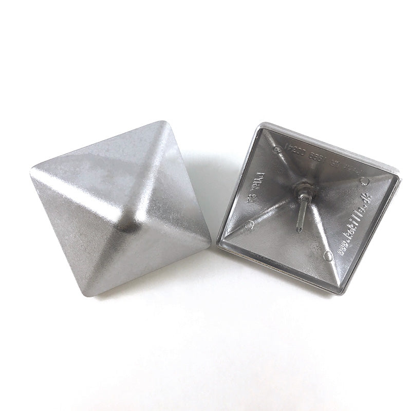 Two Quick Cap Aluminum pyramid-shaped objects are shown. One stands upright with its square base inscribed with text, while the other lies on its side, displaying its smooth shape. The reflective metallic surfaces highlight their decorative potential as post caps.