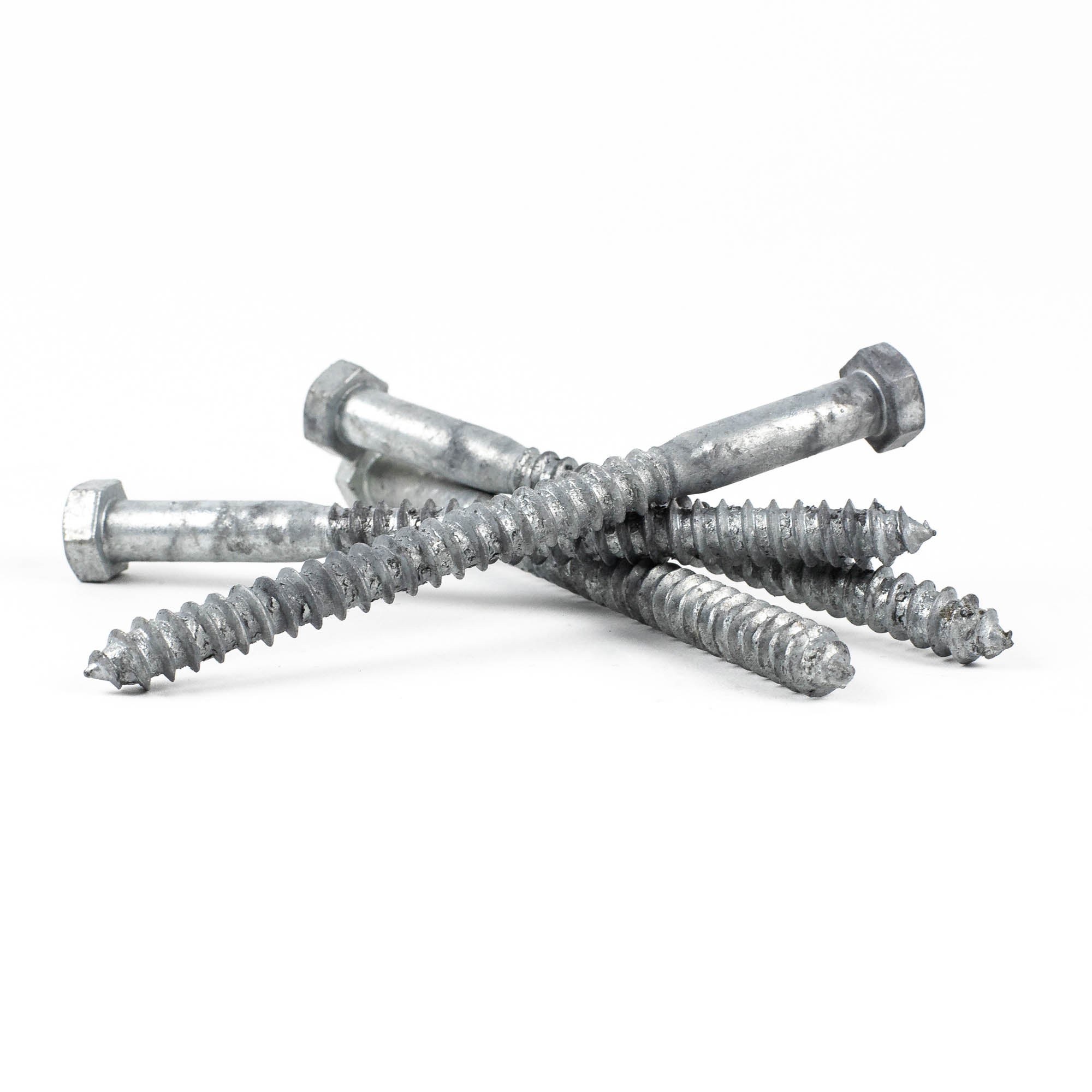 Four 3/8x5 Galv. Hex Head Lag Screws are scattered on a white background, showcasing their coarse threads and robust, industrial design with a crisscross arrangement that highlights their metallic texture and shine.