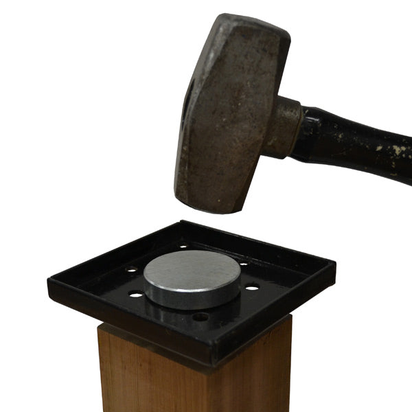 The Hammer Tool - Universal Size hovers above a metal disc on a black rectangular plate, supported by wooden post anchors, set to impact against a plain white background.