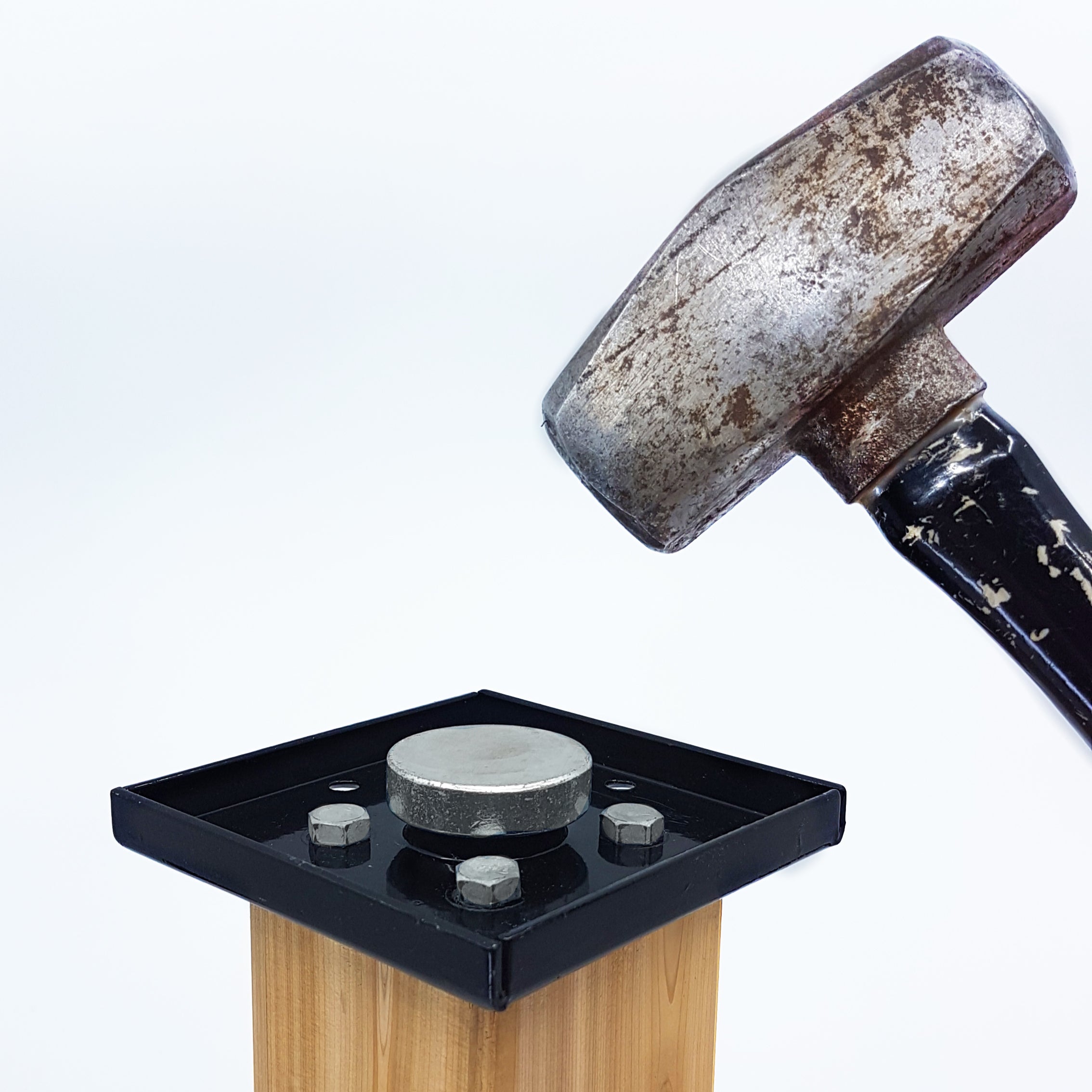 The Hammer Tool - 44 is placed on a flat, metallic surface resembling an anvil, securely mounted with a sturdy 4x4 post anchor on a wooden base, all set against a plain white background.