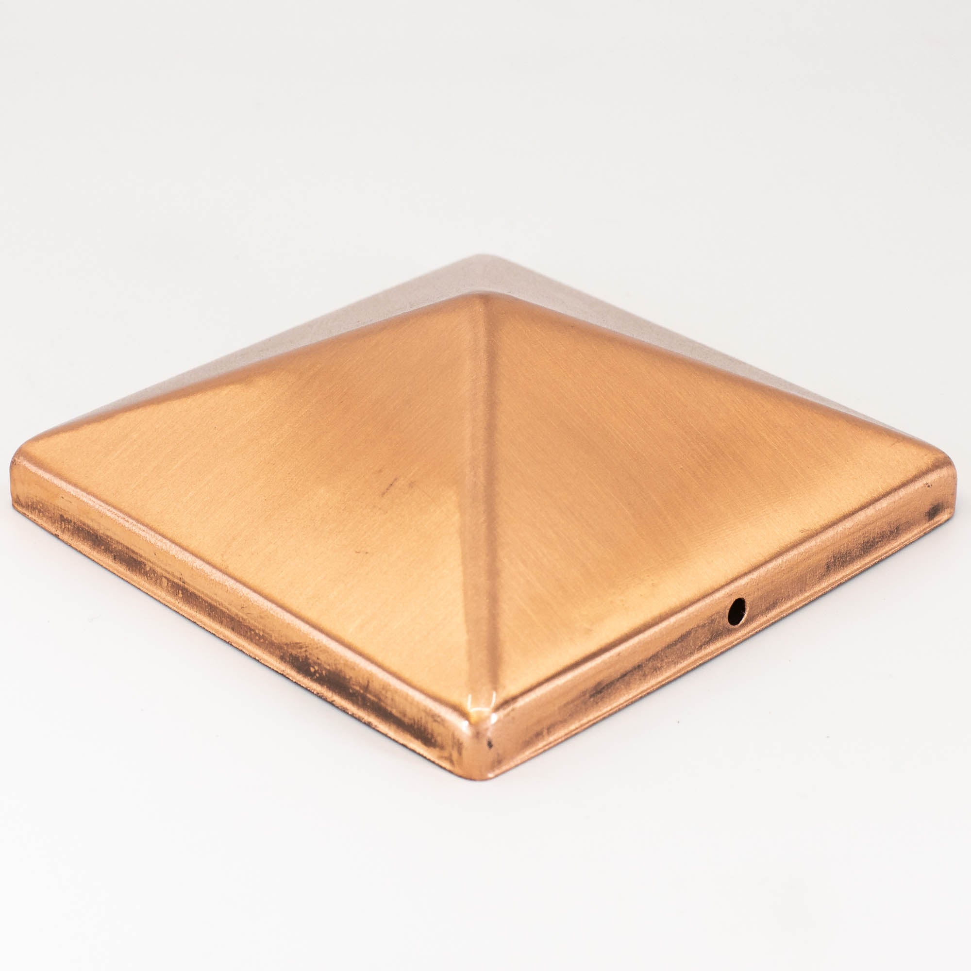 The Pyramid Metal Post Cap is a square, pyramid-shaped copper cap with a smooth, shiny finish. It features a small hole on one side and stands out beautifully against a plain white background.
