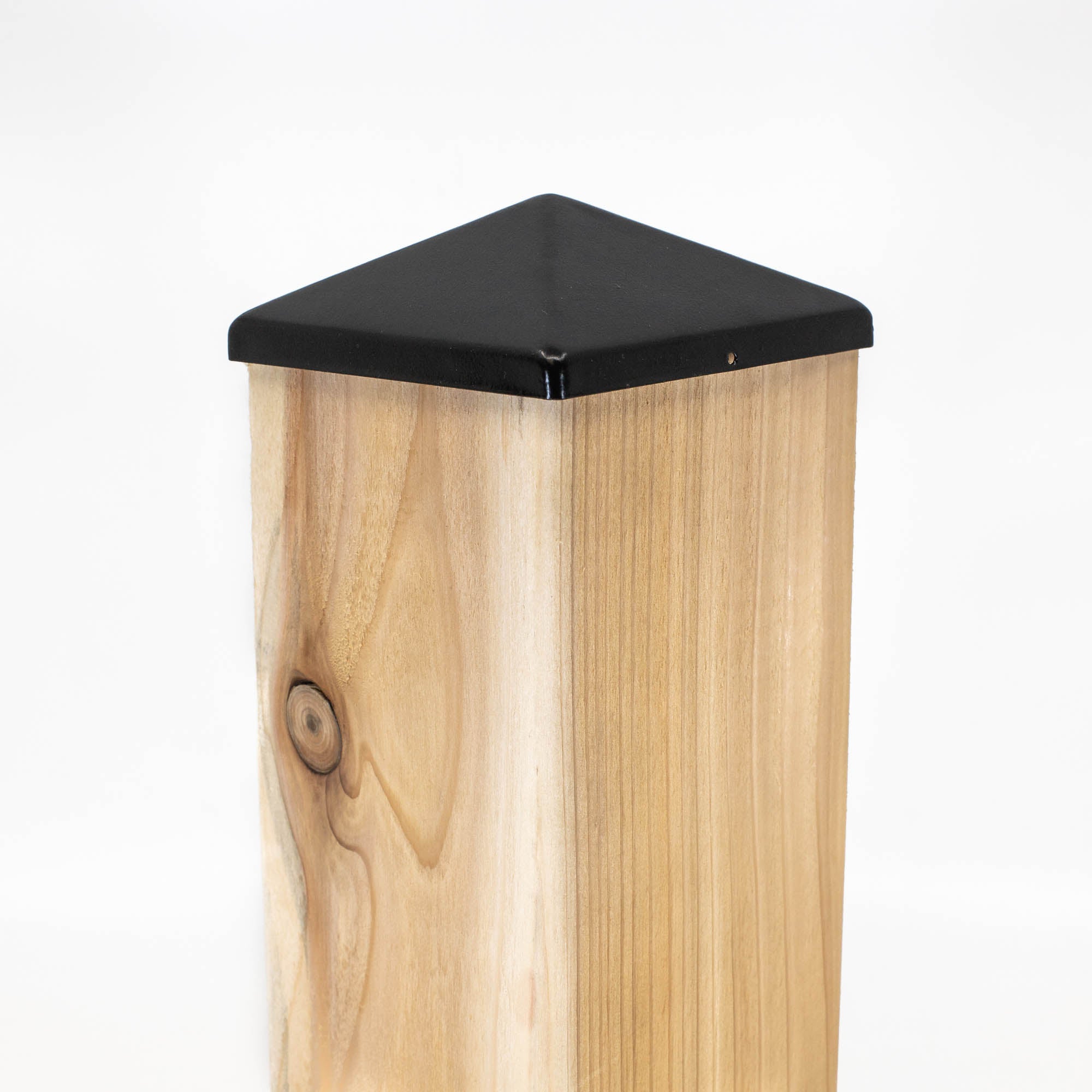 A Titan BP wooden fence post with a sleek Pyramid Metal Post Cap. The visible wood grain and knot add natural charm, contrasting perfectly with the glossy black cap. Set against a white background, it highlights both durability and style.