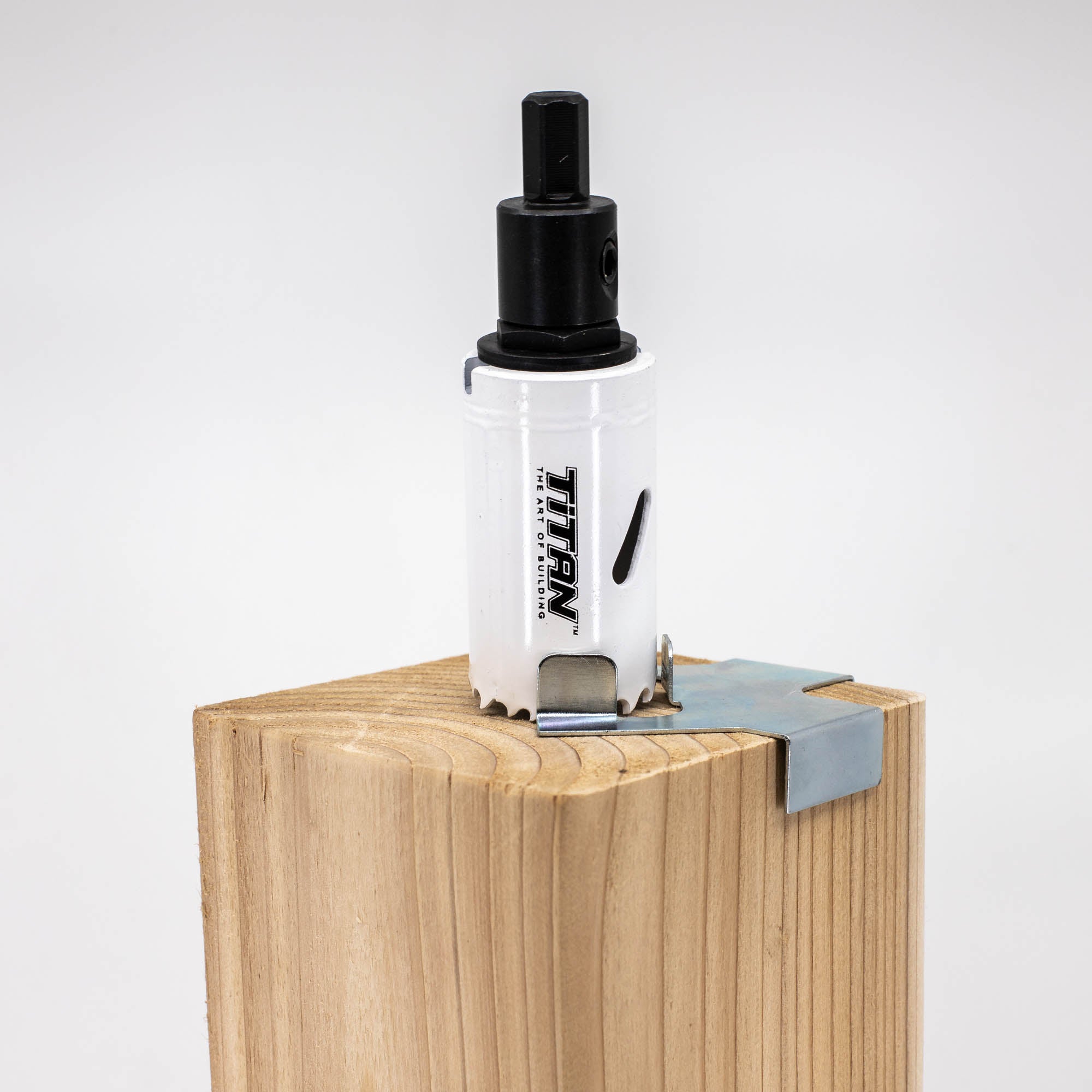 A Hole Saw & Arbor is attached to a drill bit on the corner of a light wood block, with a metal corner bracket and guide rod below, showcasing precise woodworking.
