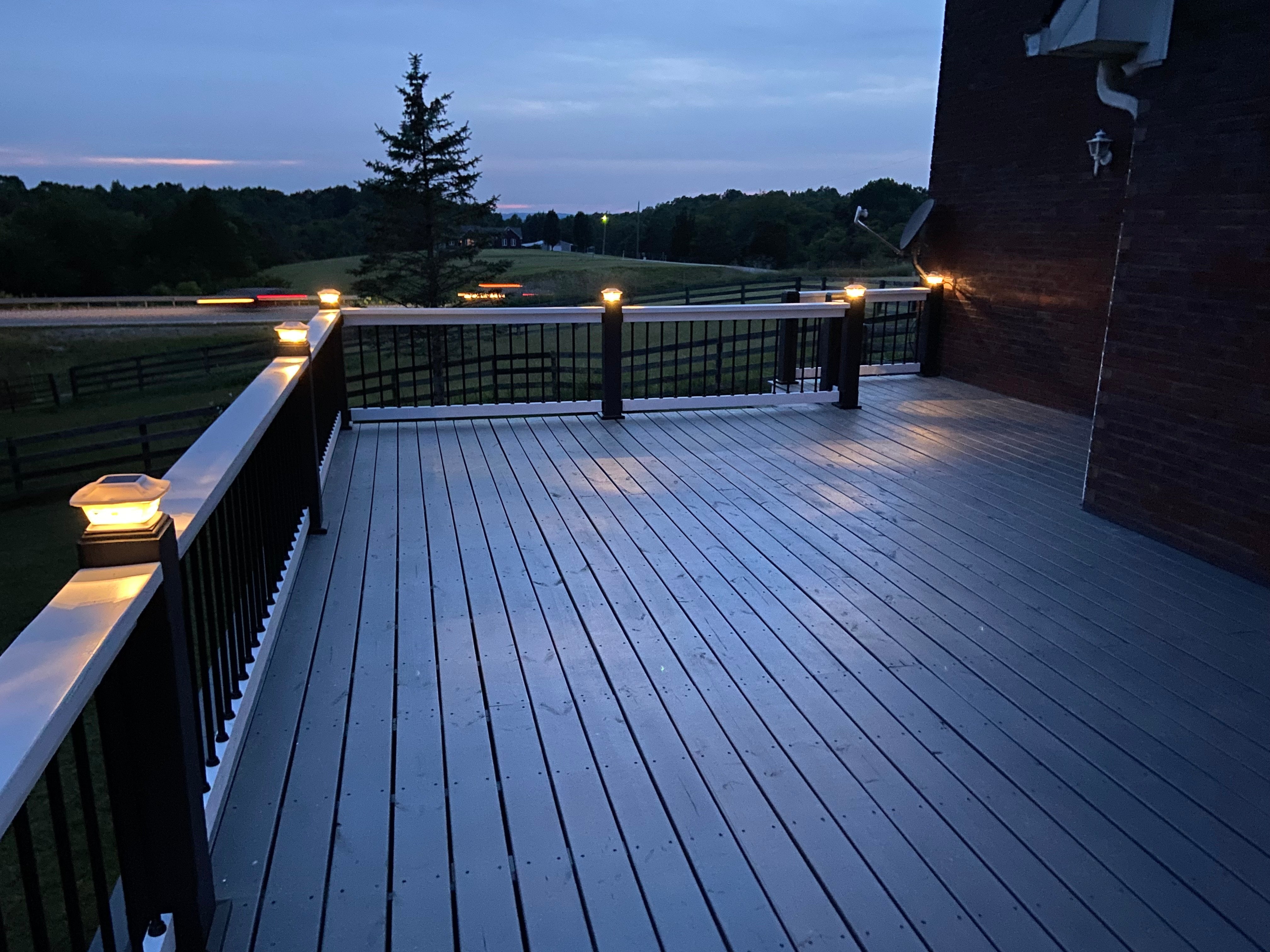 Wooden deck at night with string lights and a view of trees and fields.
