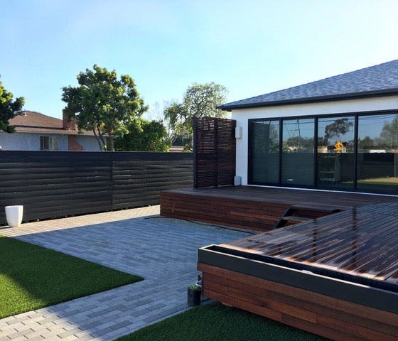 Modern outdoor patio with wooden furniture and a black fence.