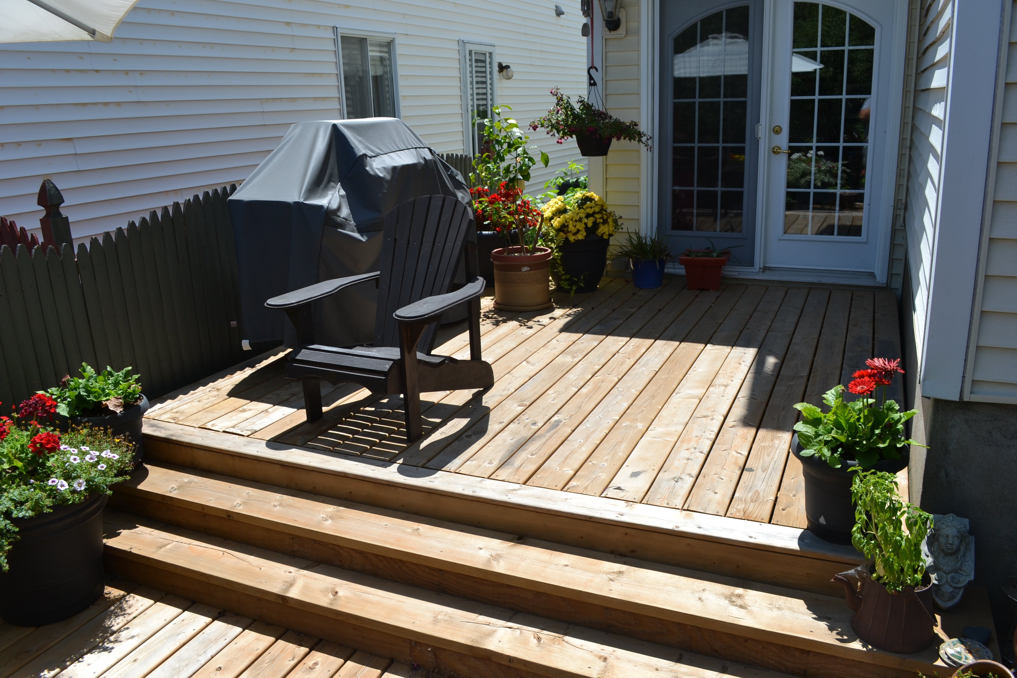 Backyard deck with chairs, potted plants, and a grill cover.