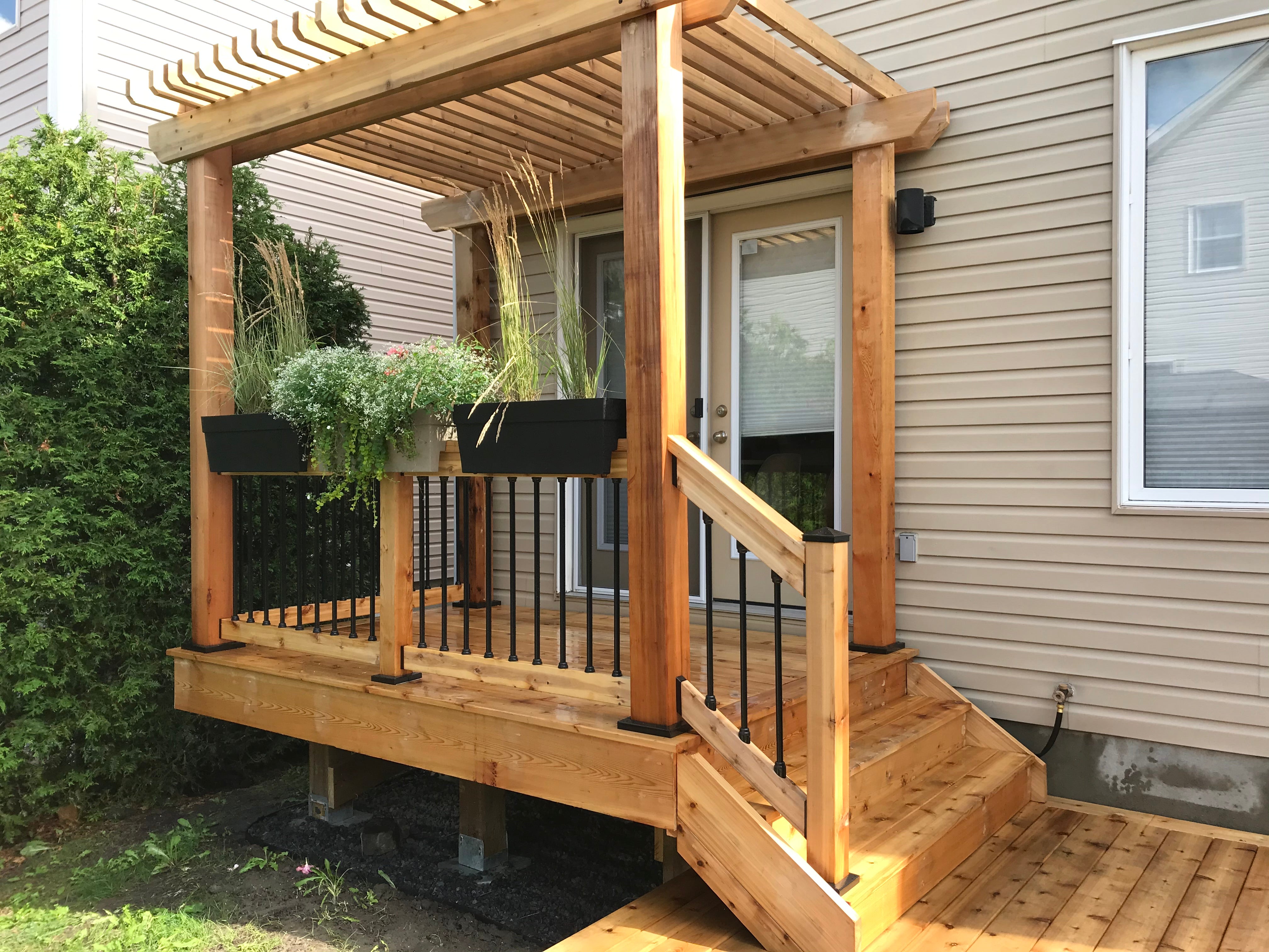 Wooden deck with pergola and plants, attached to a house.