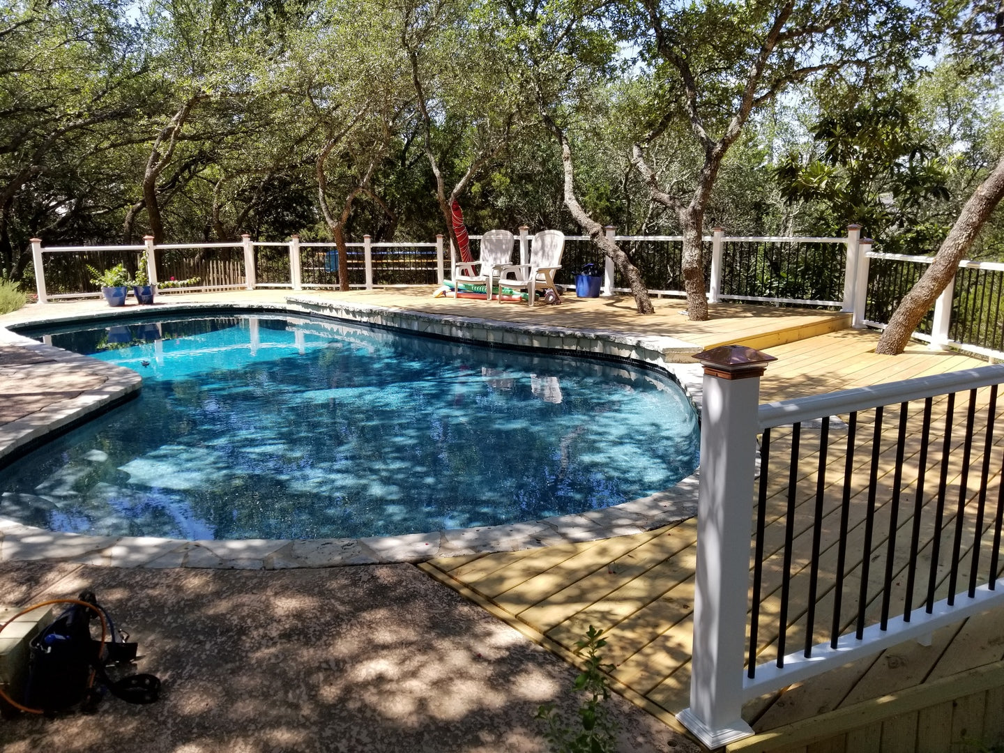 Pool area with deck, trees, and a fence