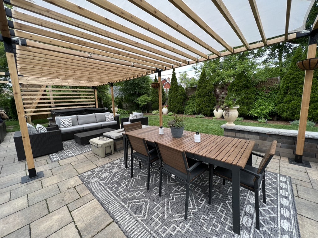 Outdoor patio with wooden pergola, table, chairs, and outdoor furniture on a stone patio.