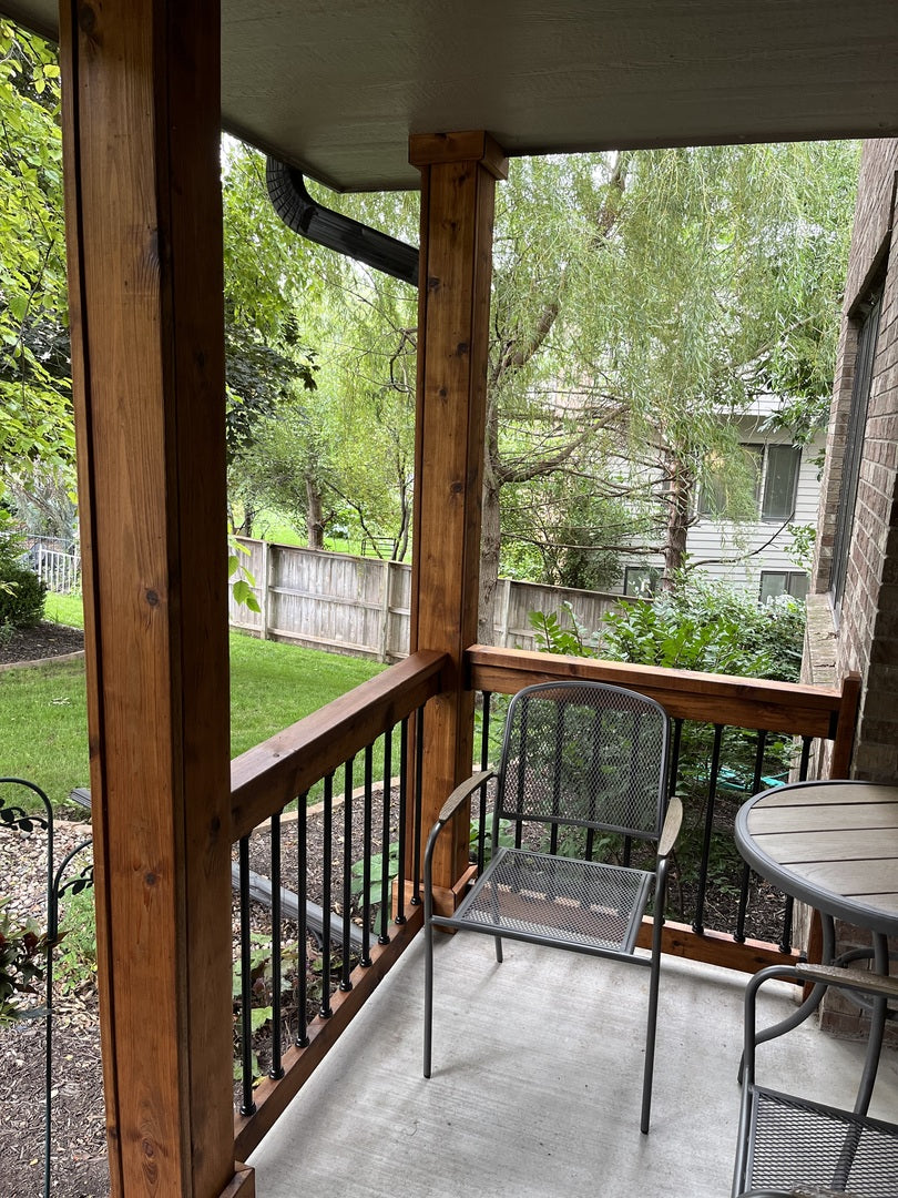 Balcony with chairs and a table, looking out onto a garden and trees.