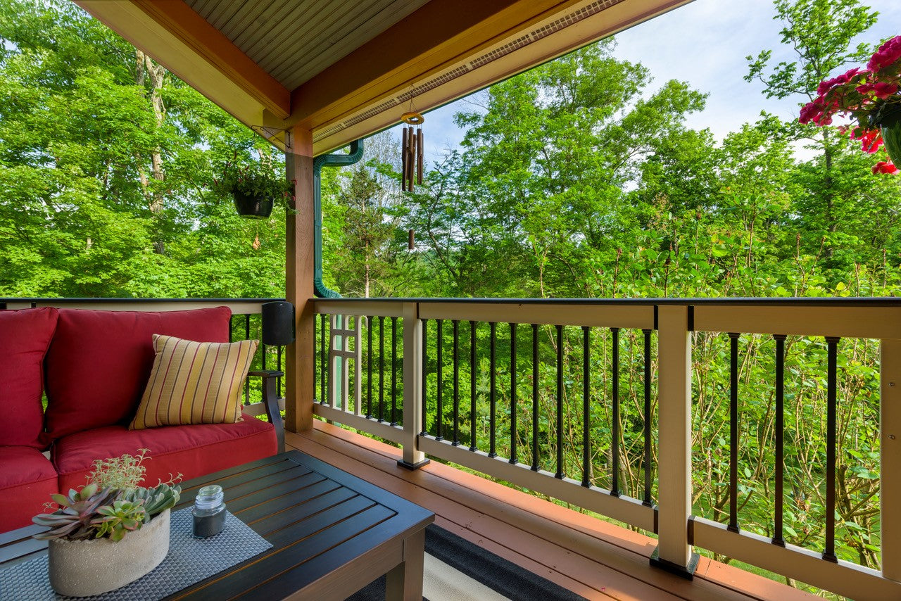 Balcony with red sofa, table, and view of green trees