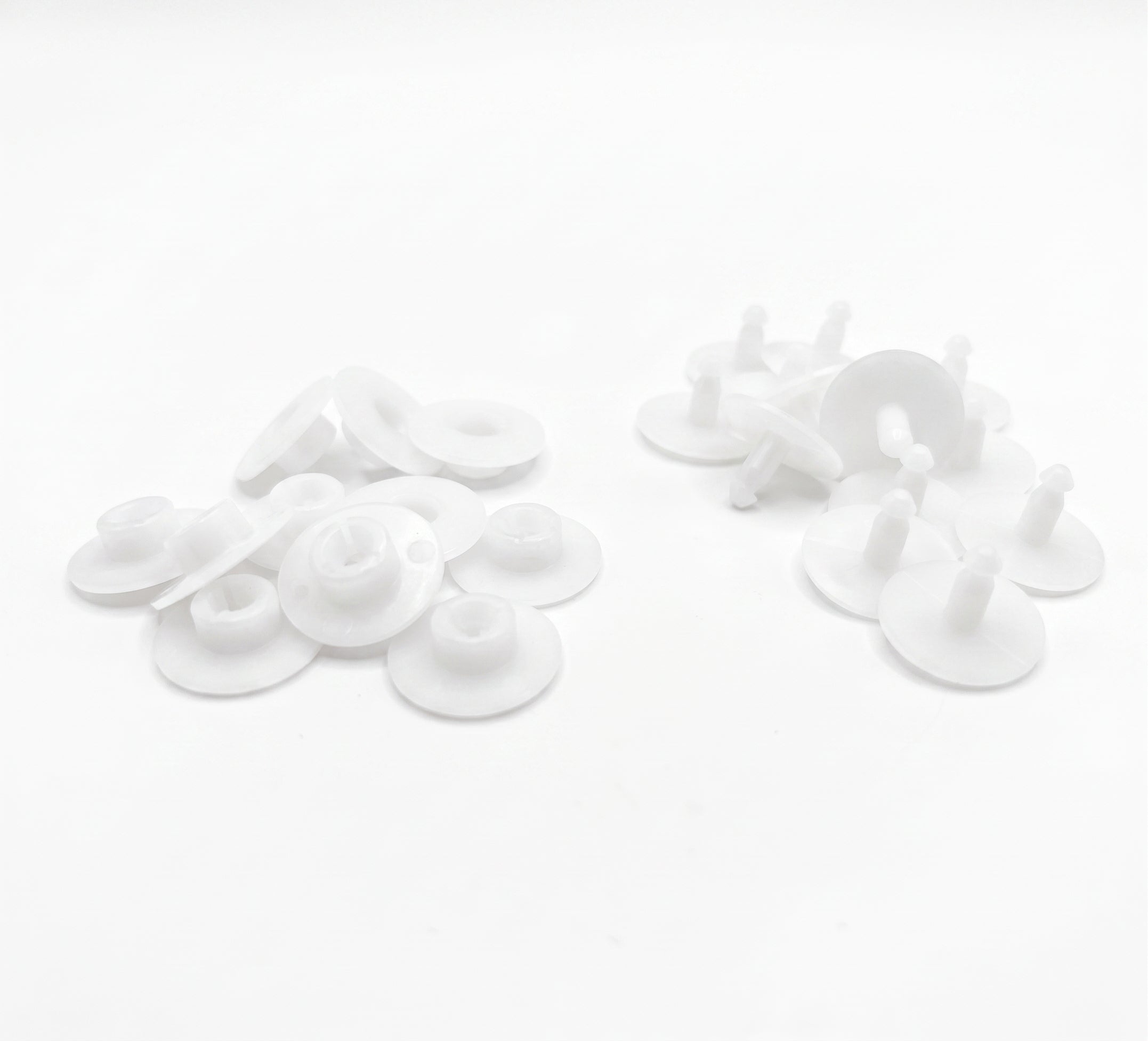 White plastic snap fasteners and grommet-like hardware pieces arranged on a plain white background.